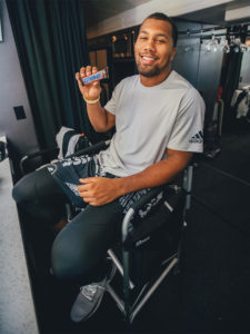 1UP Sports Marketing client Bradley Chubb sits in a chair holding a Snickers bar