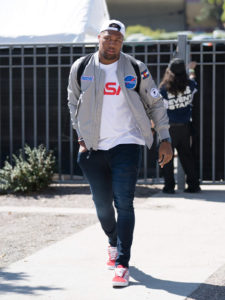 1UP Sports Marketing client Bradley Chubb walks with purpose, wearing a gray jacket with a "Snickers" and "Astronaut" patch